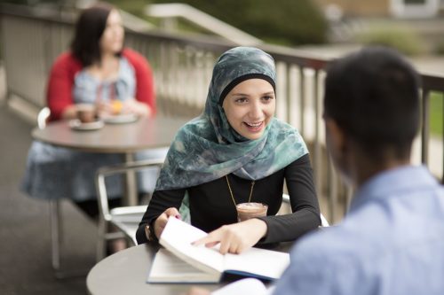 A young woman in a headscarf discusses with a colleague over coffee.